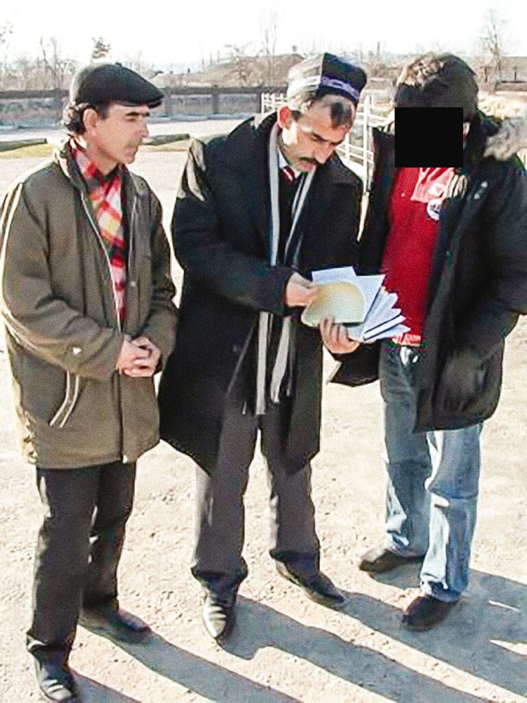 three people stand together outside and one is holding a bible 