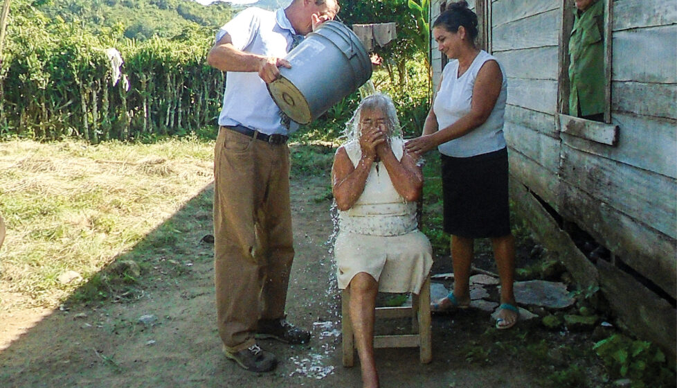 A man pours water over the head of a woman for baptism