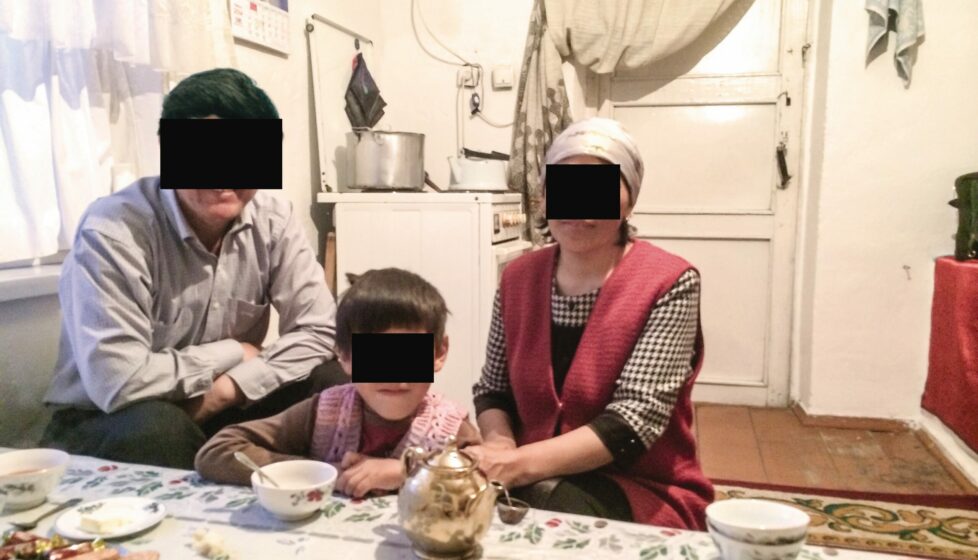 family of three sit in their kitchen with black boxes over their faces