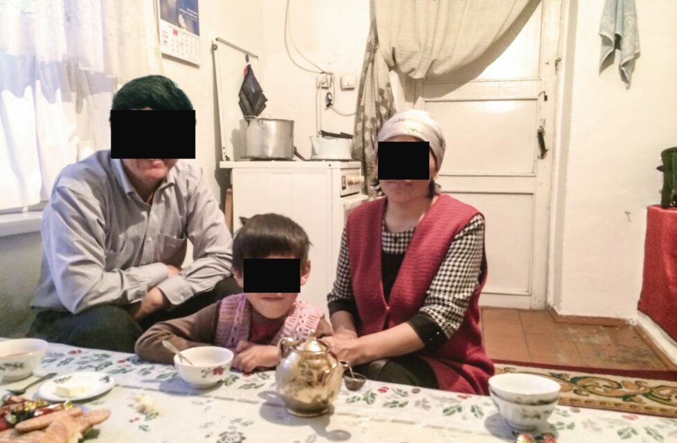 family of three sit in their kitchen with black boxes over their faces