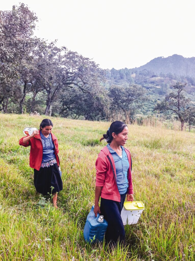 two women carrying water and supplies through a field 