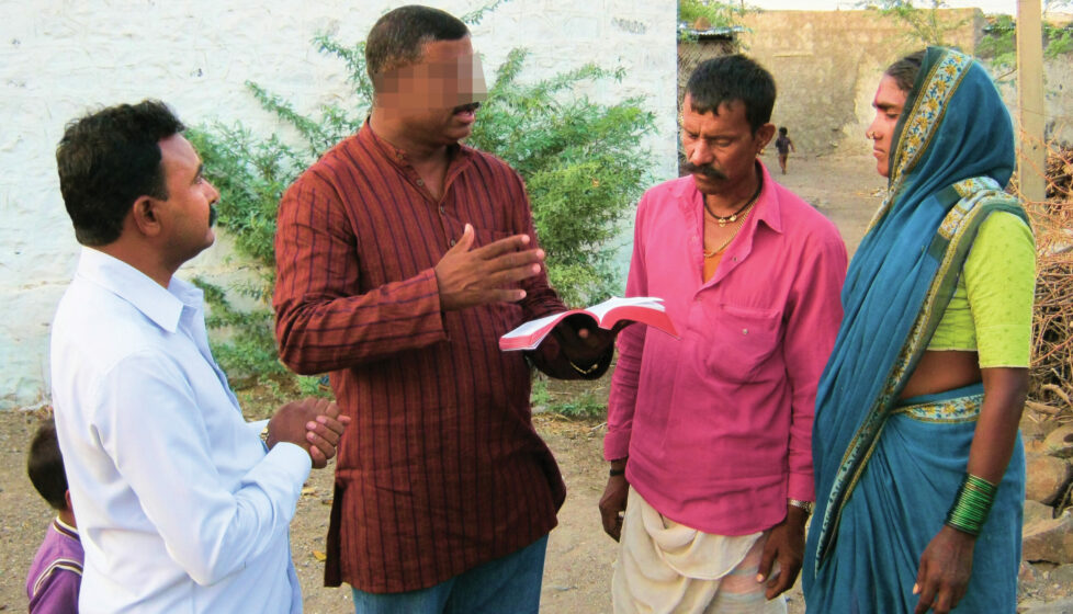 a man stands reading the bible to three other people