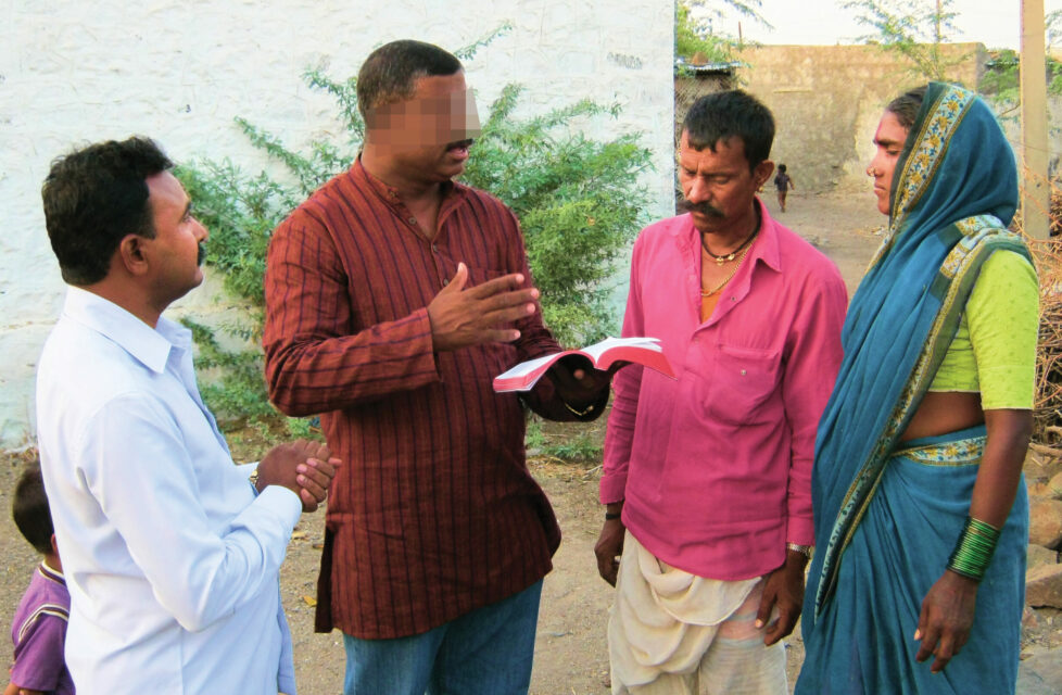 a man stands reading the bible to three other people