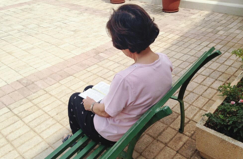 a woman sits on a bench outside reading her bible