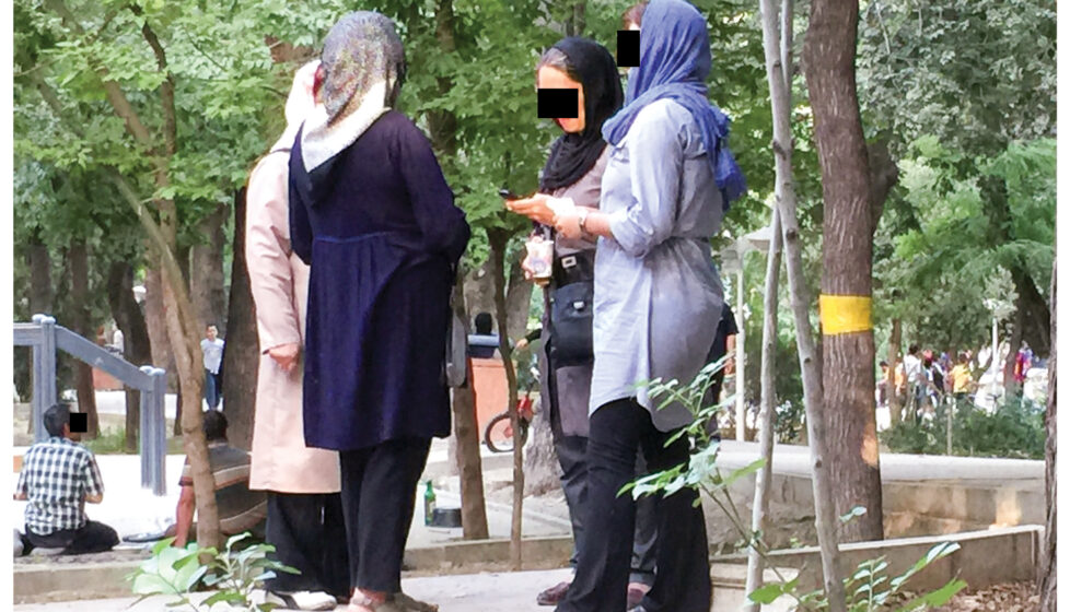 a group of women stand together outside talking with black boxes over their eyes