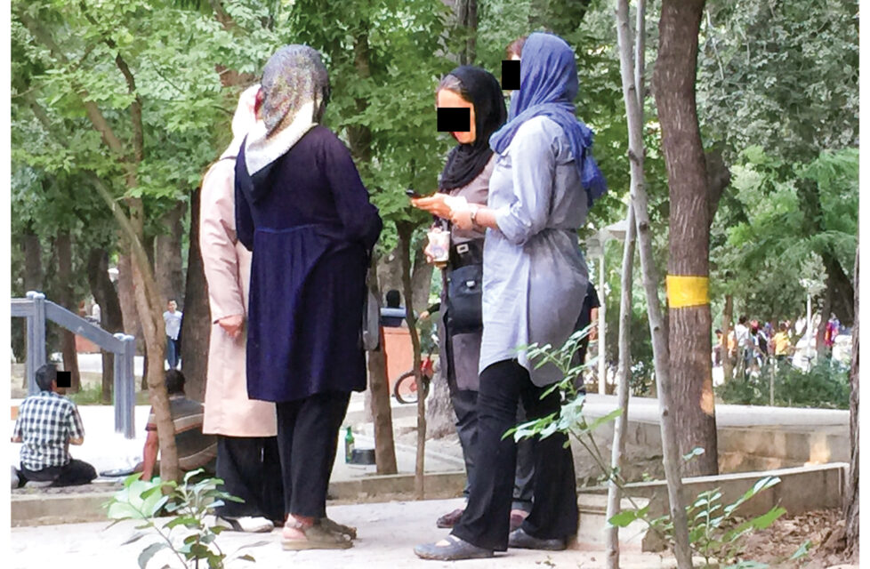 a group of women stand together outside talking with black boxes over their eyes