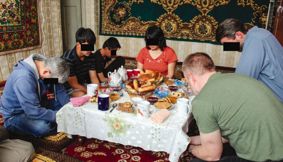 a Christian family in Central Asia sits at their table praying over their meal