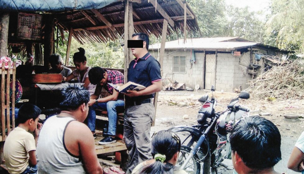a man reads the bible to a group of men outside in their village