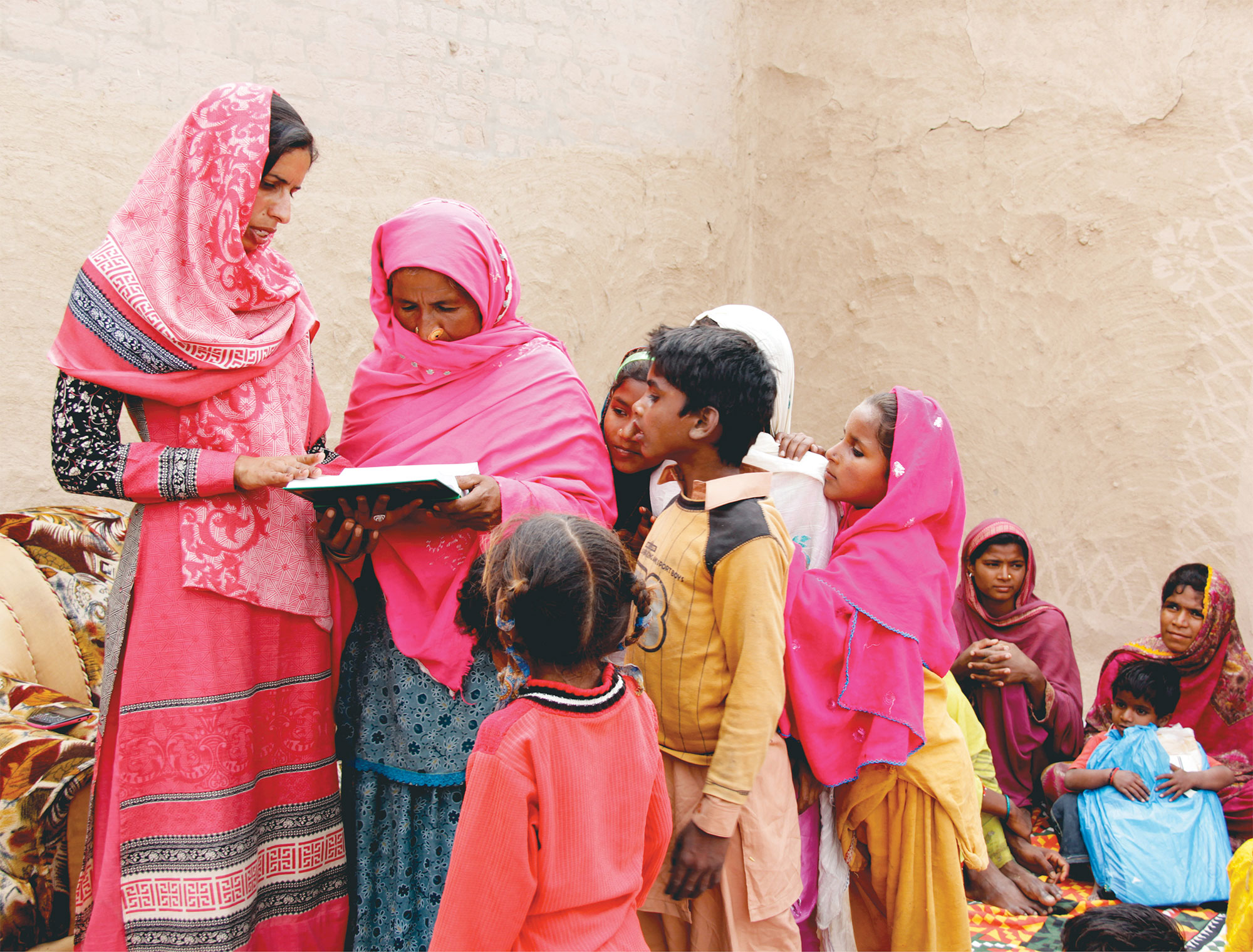 Two women and a group of younger children poring over a bible