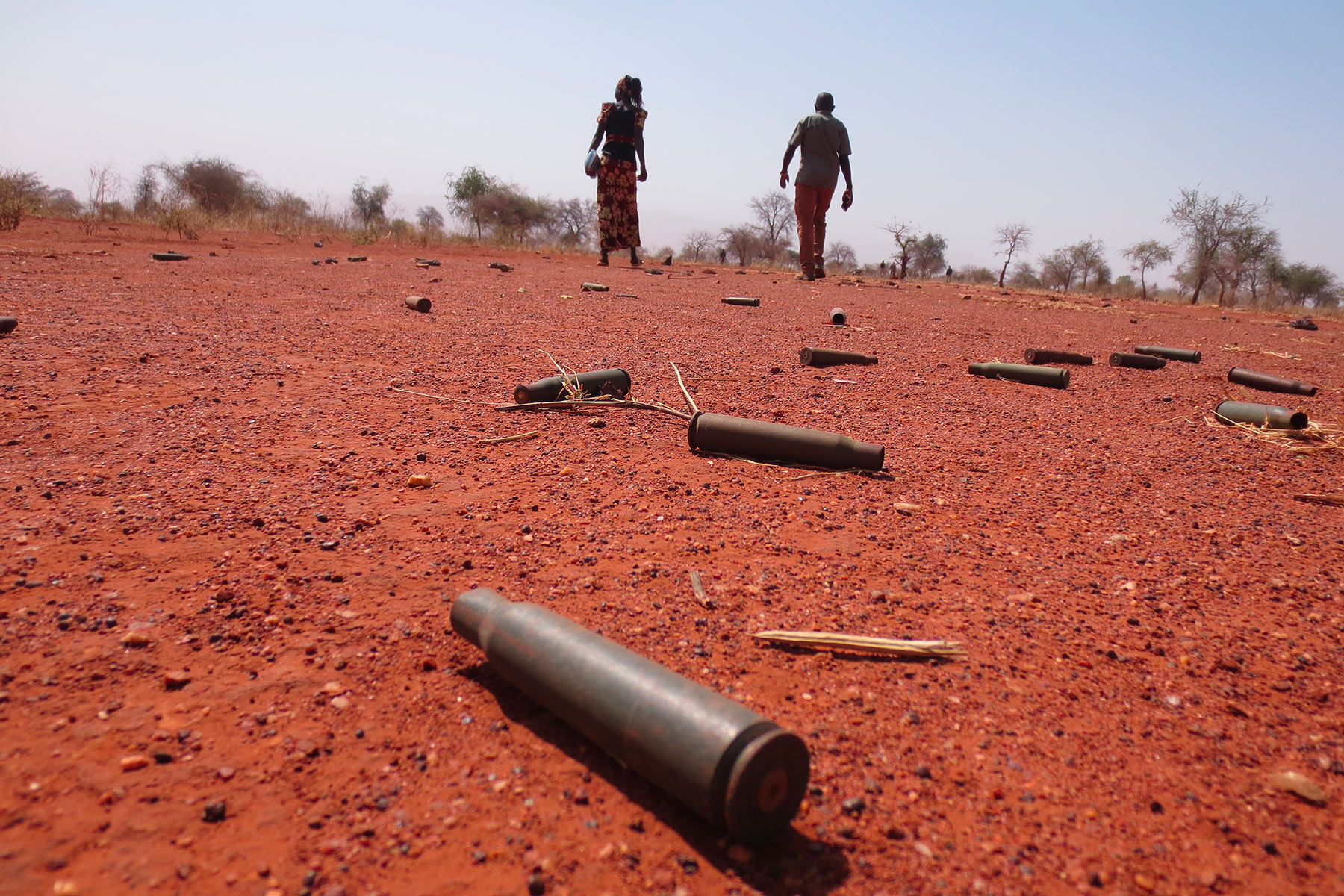 Two people walking across ground littered with bullet casings