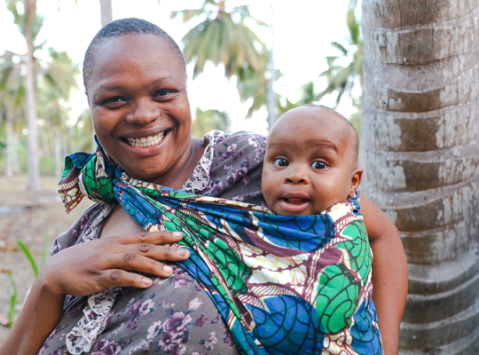 Woman and baby smiling next to a tree