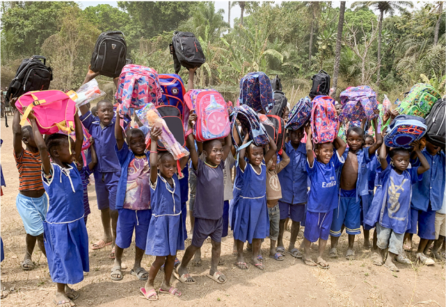 Grupo de niños sosteniendo mochilas sobre sus cabezas