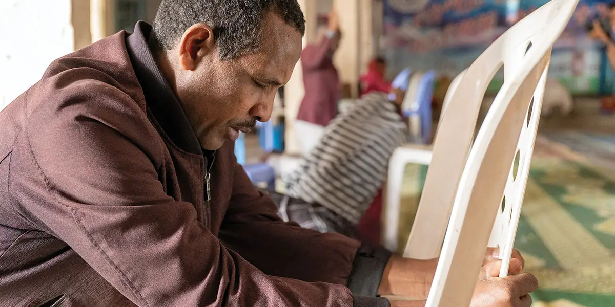 Man holding white chair, praying