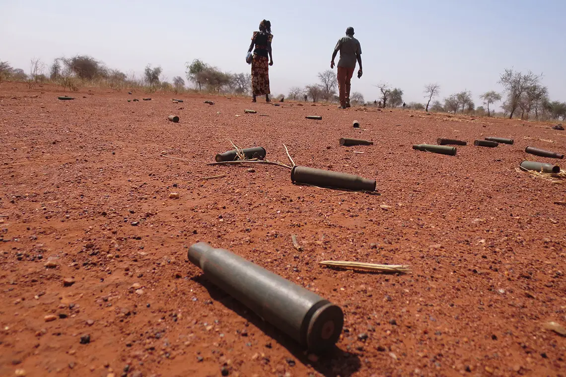 Two people walking through field littered with bullet casings