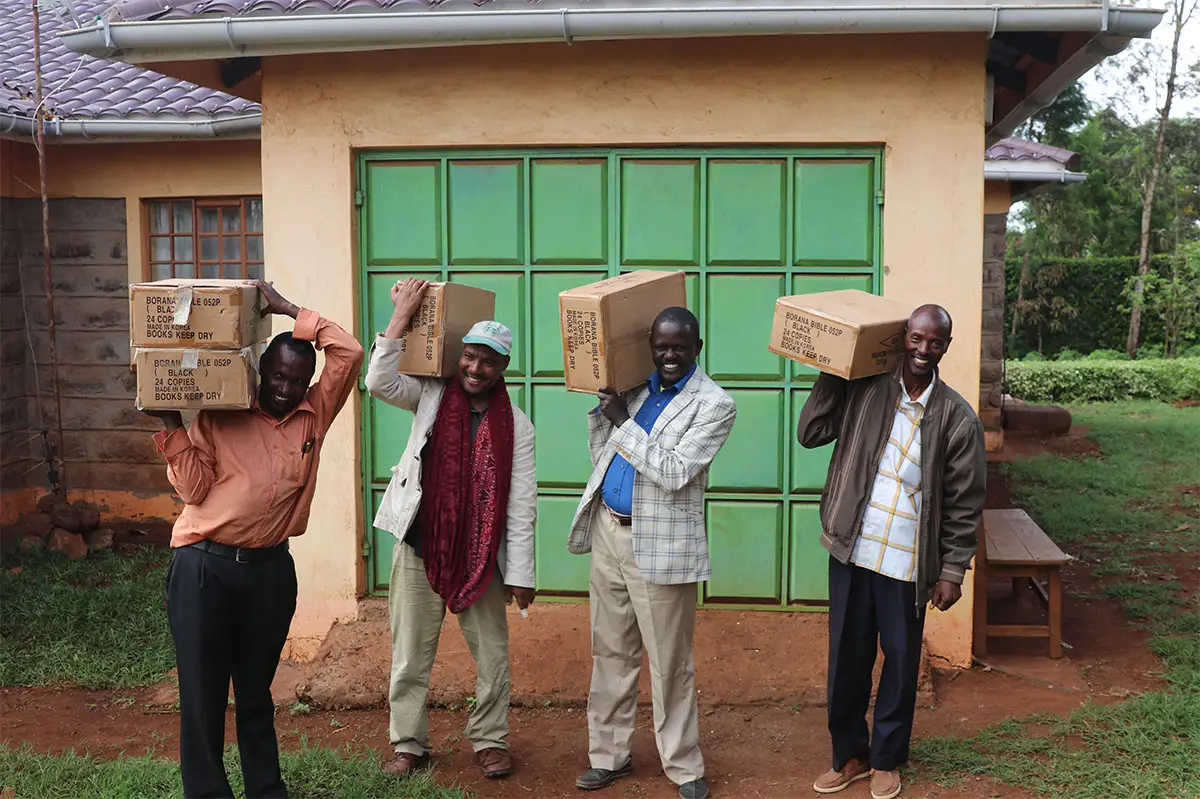 People holding up boxes of Bibles in front of garage