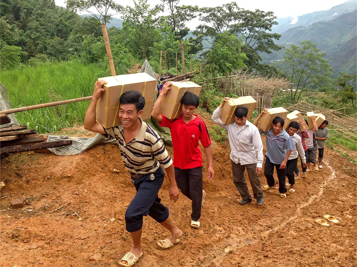 Grupo de personas cargando cajas de Biblias hasta una colina fangosa