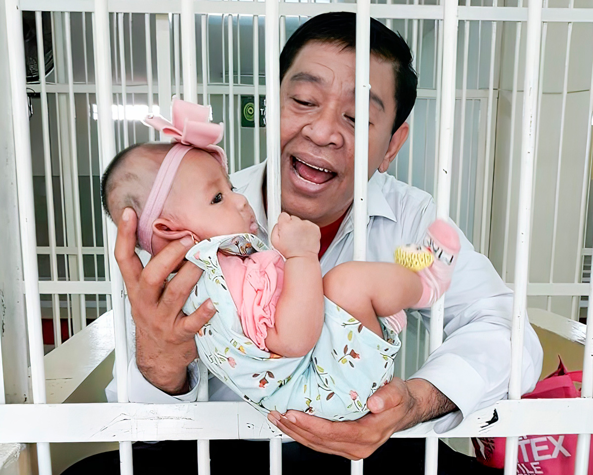 Man smiling holding baby between jail bars