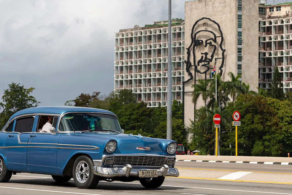 Blue car in front of building with art depicting Che Guevara on the side