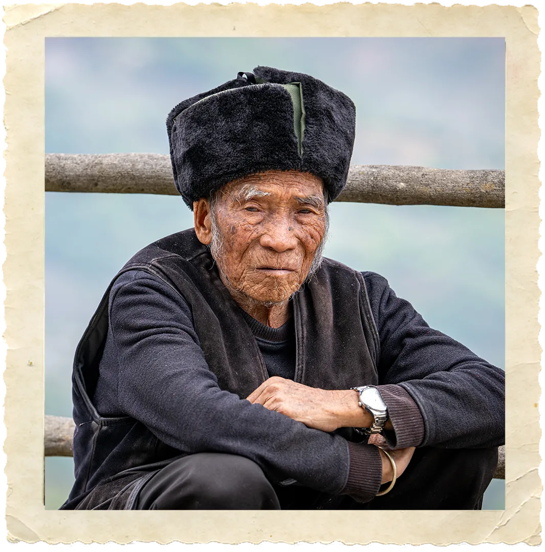 Older man sitting in front of wood fence