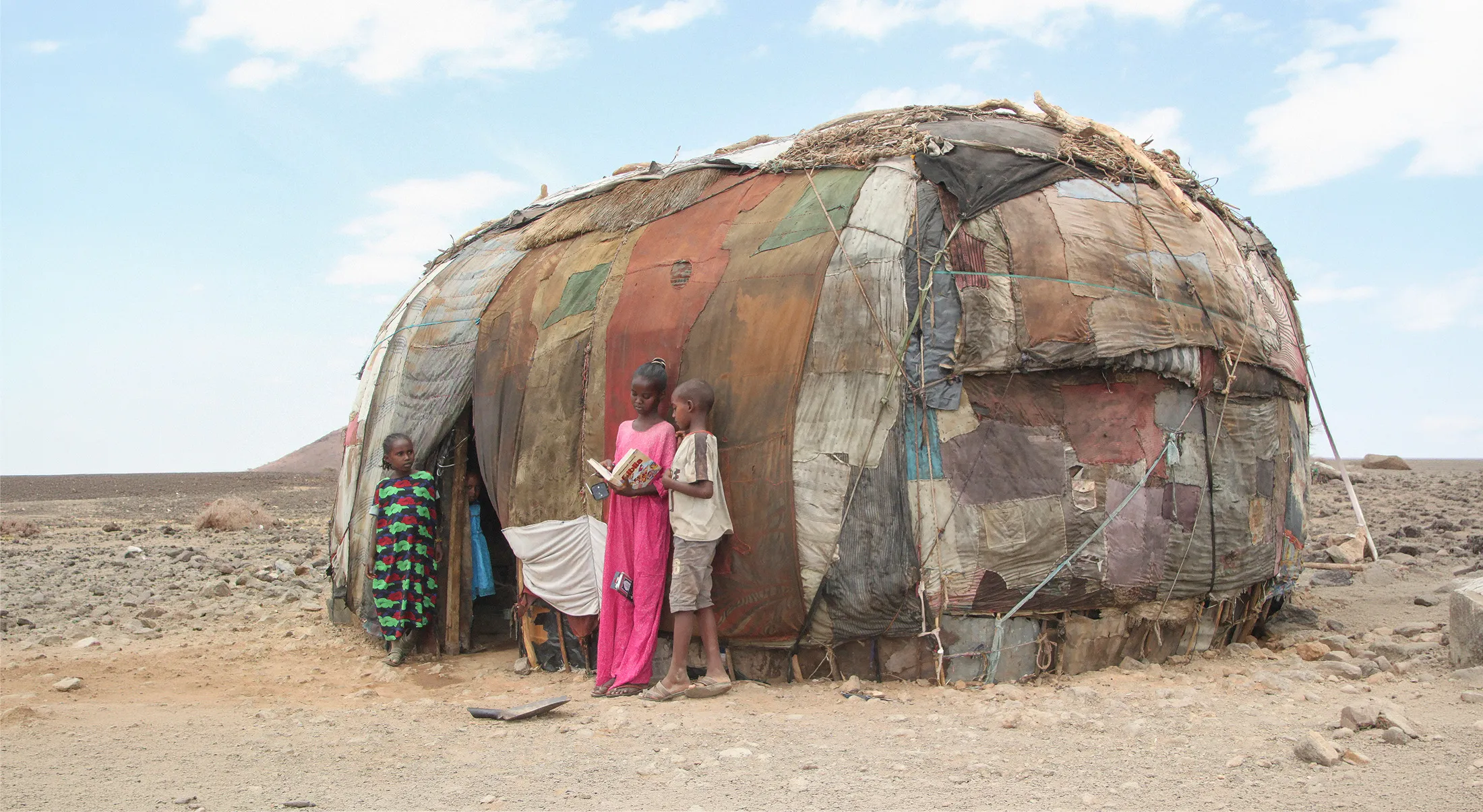 Children reading a Bible outside their shelter