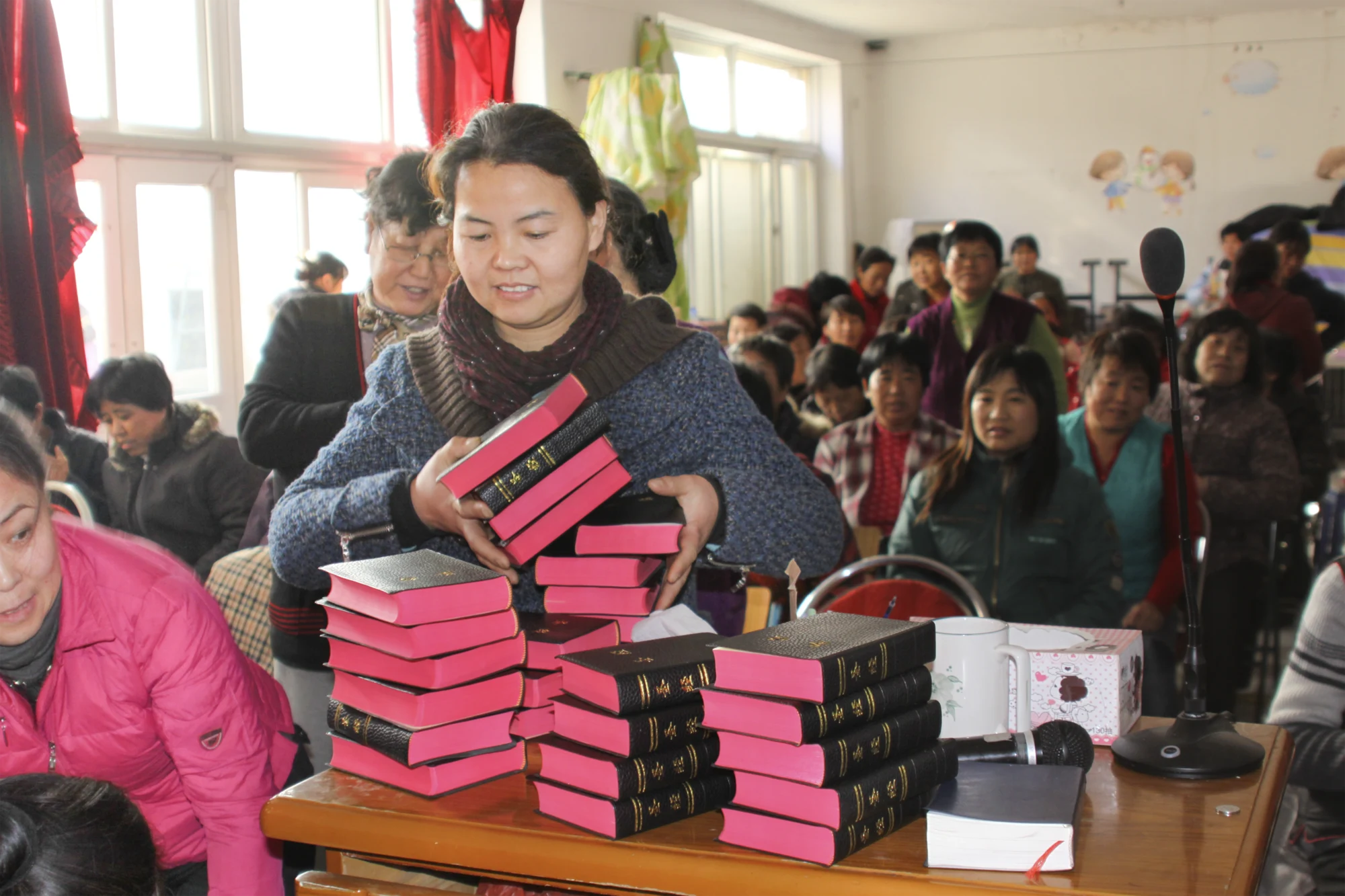 A woman holding a stack of Bibles among fellow believers