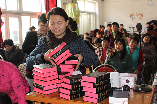 Woman taking a bible from a large stack in a full church