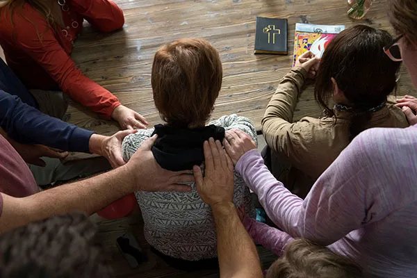 Christians gathered around a seated woman in prayer