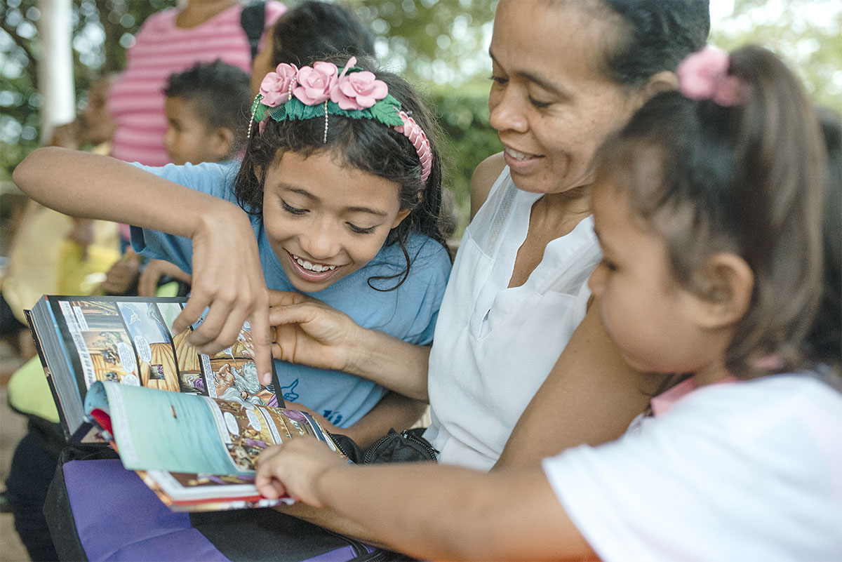 Children gathered around and reading a graphic Bible
