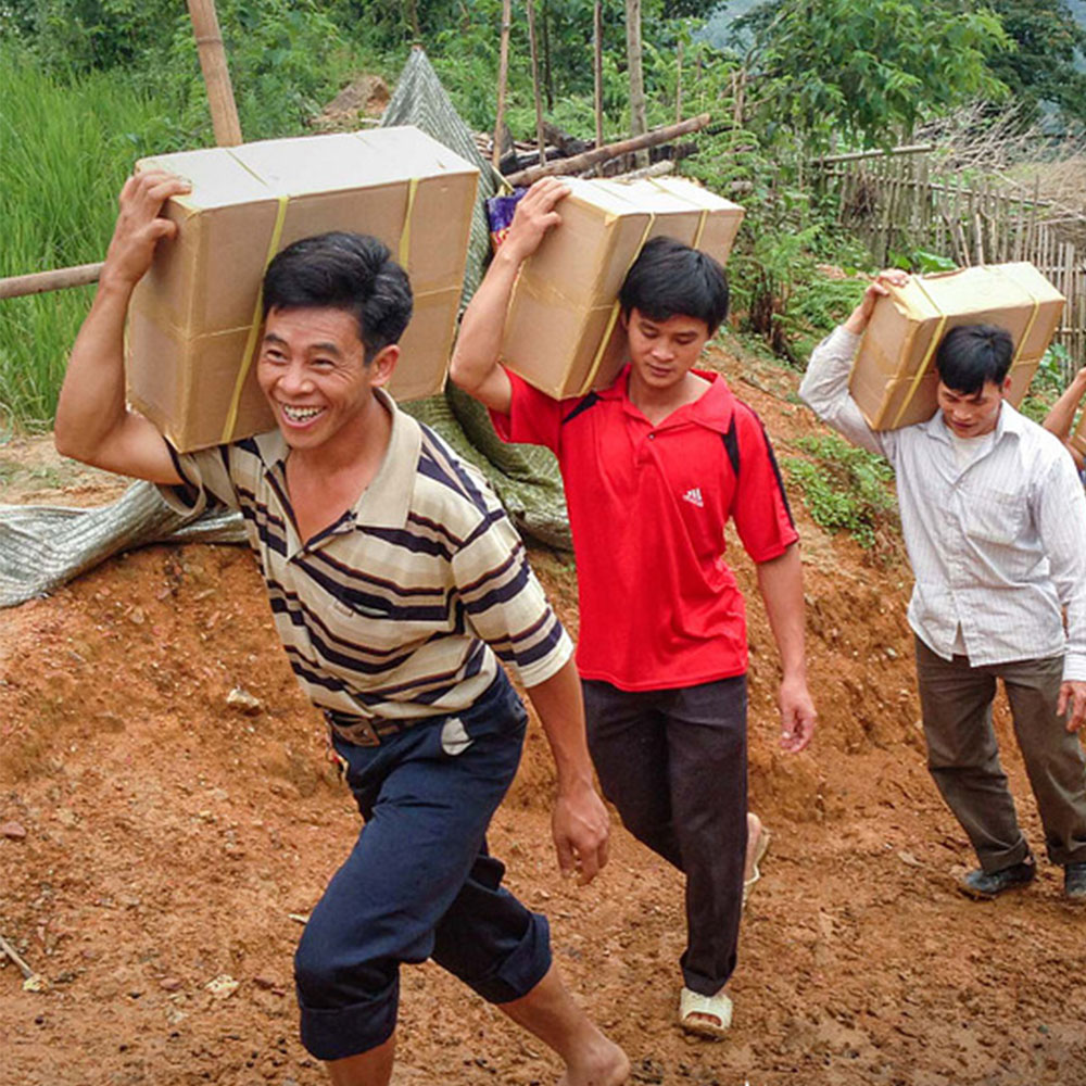 People carrying boxes up dirt path