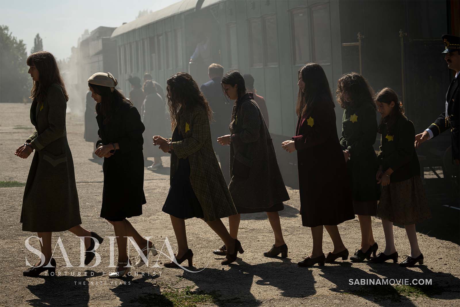 Line of handcuffed women with yellow stars pinned to their coats being marched across train platform.