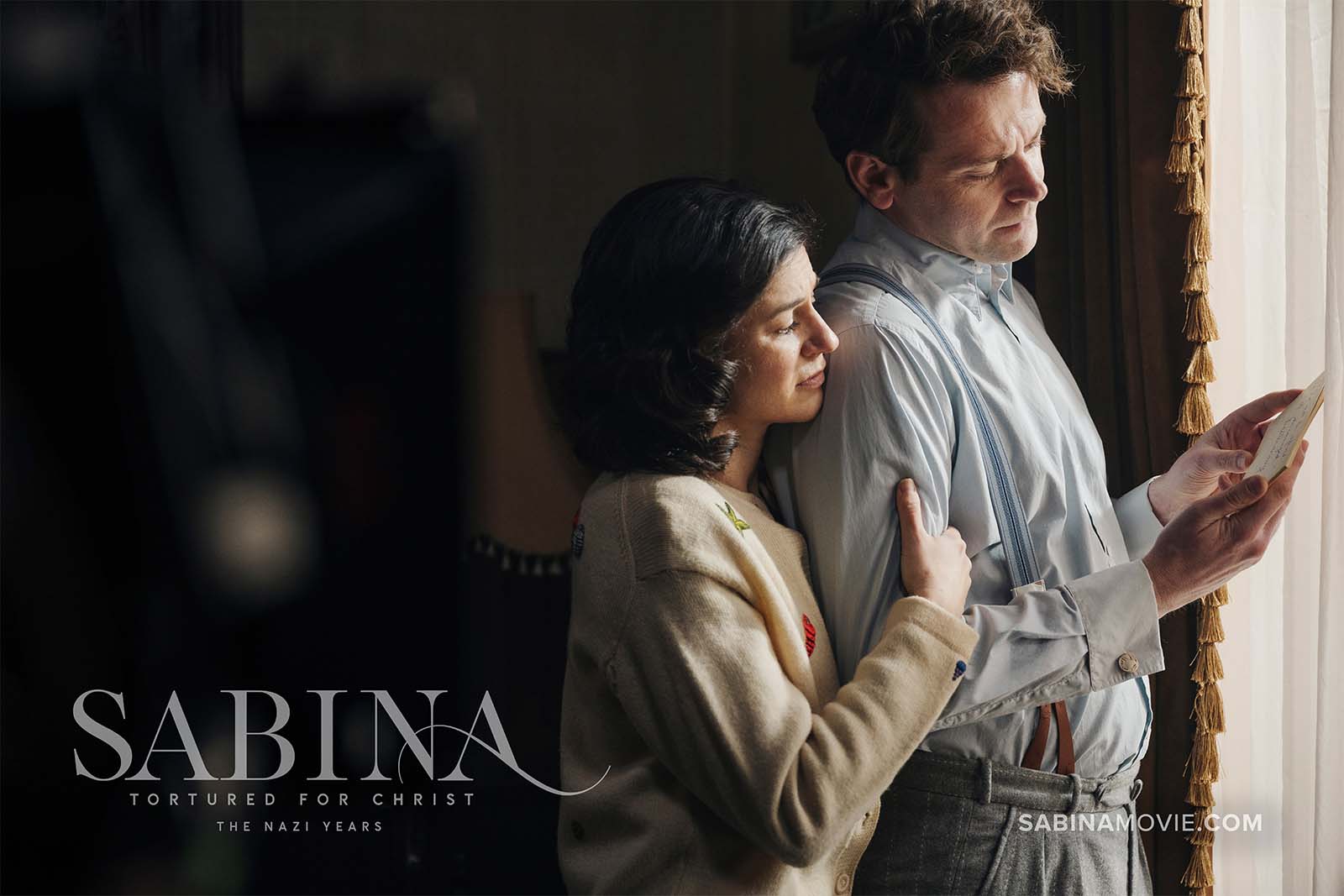 Sabina and Richard standing in front of window reading a document.