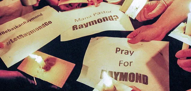 Hands holding 'pray for Raymond' signs and candles