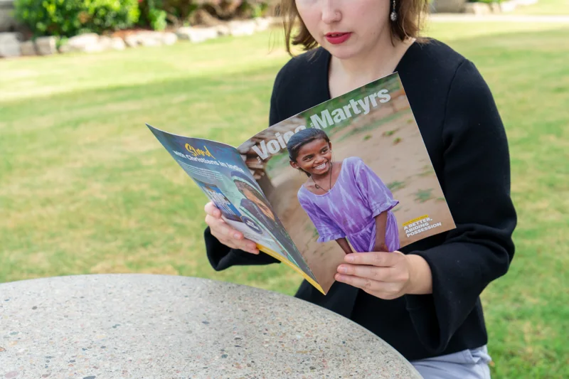 A woman reading a VOM magazine outdoors, with a young woman featured on the cover