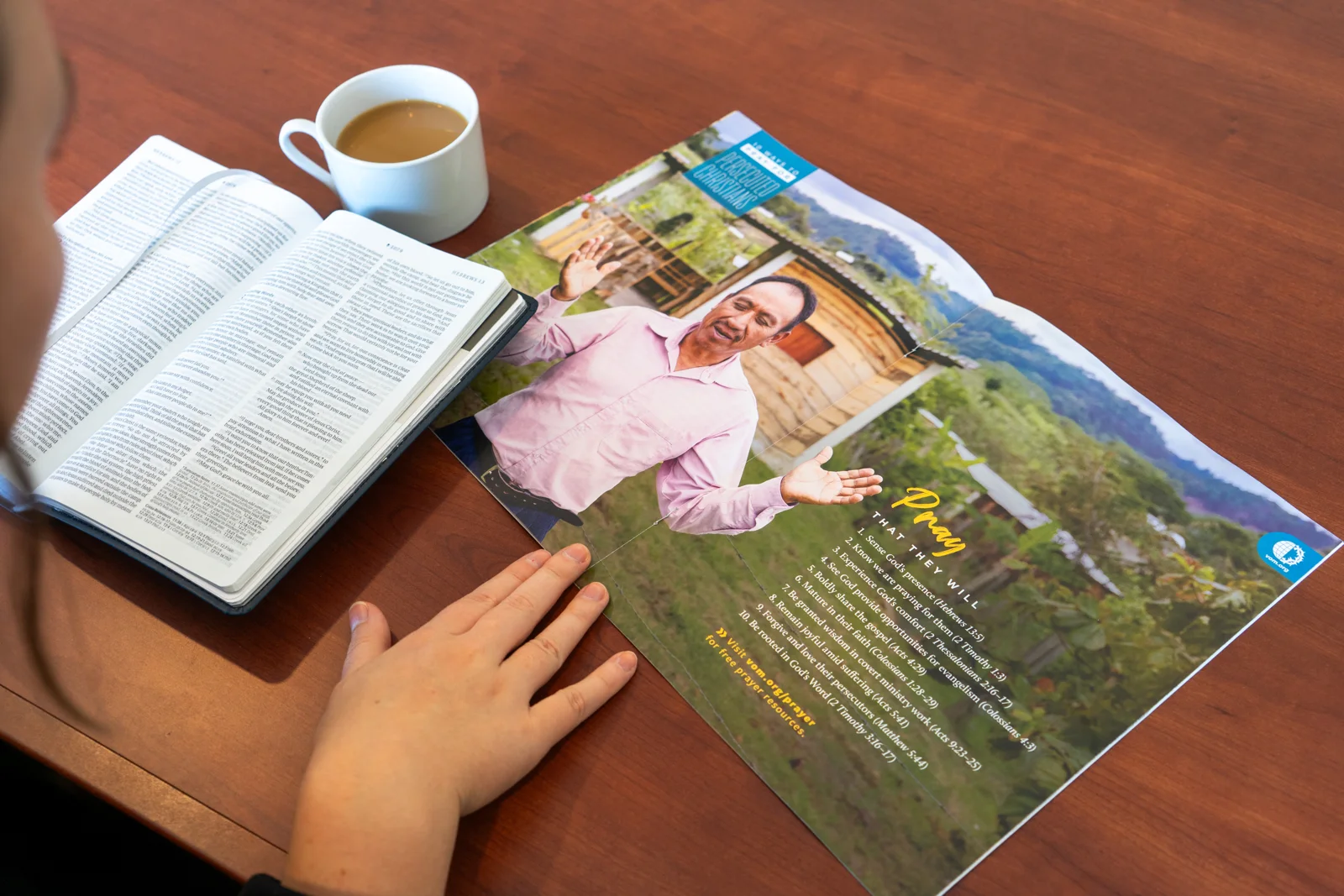 An open VOM magazine beside a Bible and a cup of coffee