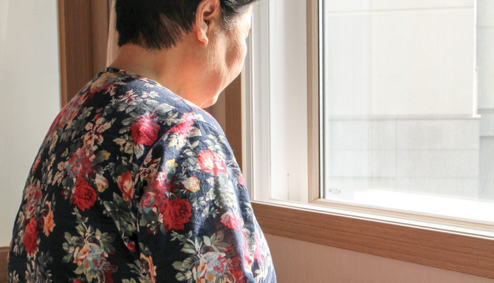 An elderly woman sits by a window