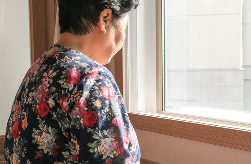 An elderly woman sits by a window