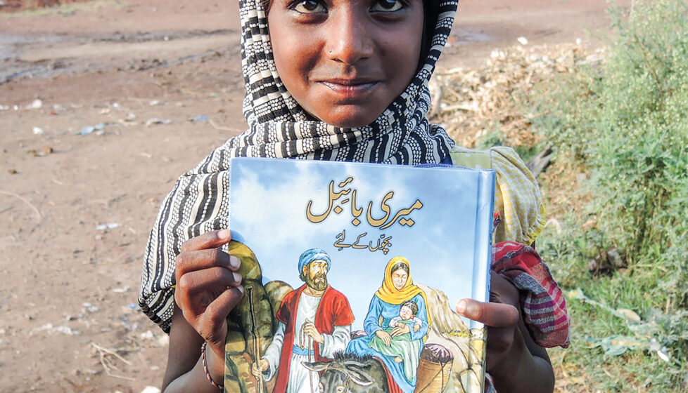 Child stands holding a bible and smiling