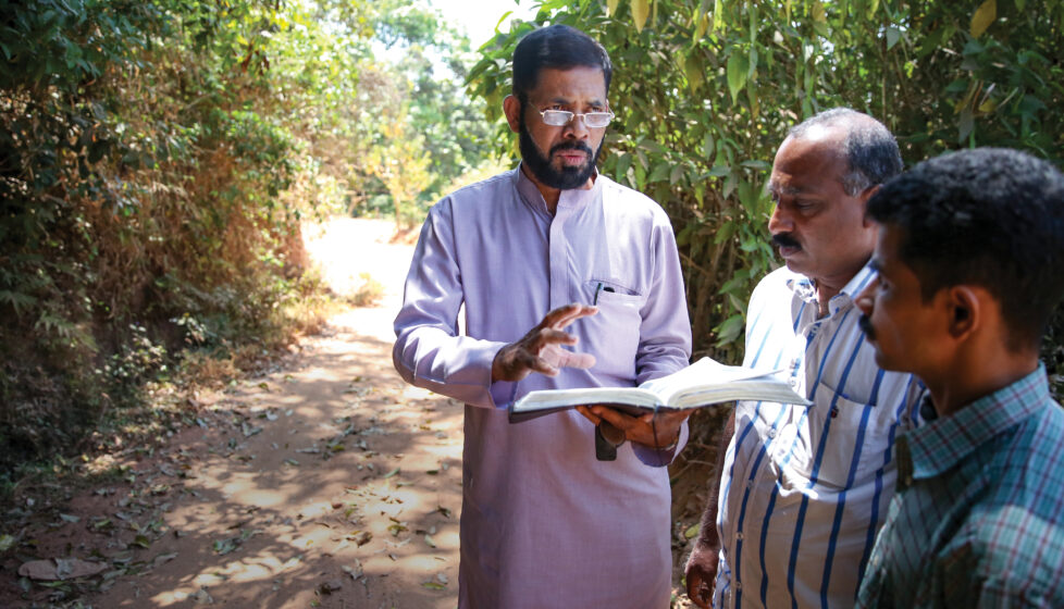 a man reads the bible to two other men outside