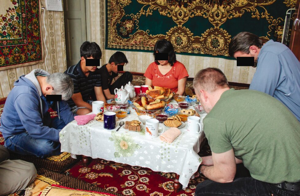 a Christian family in Central Asia sits at their table praying over their meal