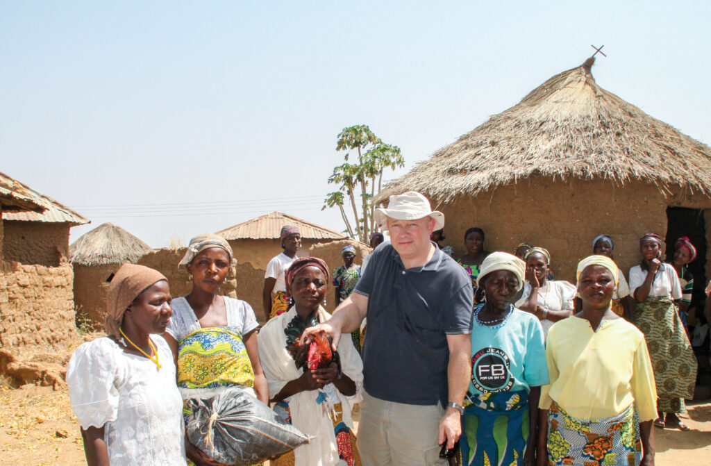 Man standing in a village with 5 people surrounding him 