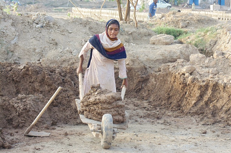 A woman rebuilding from the earthquake and moving dirt in wheelbarrow 