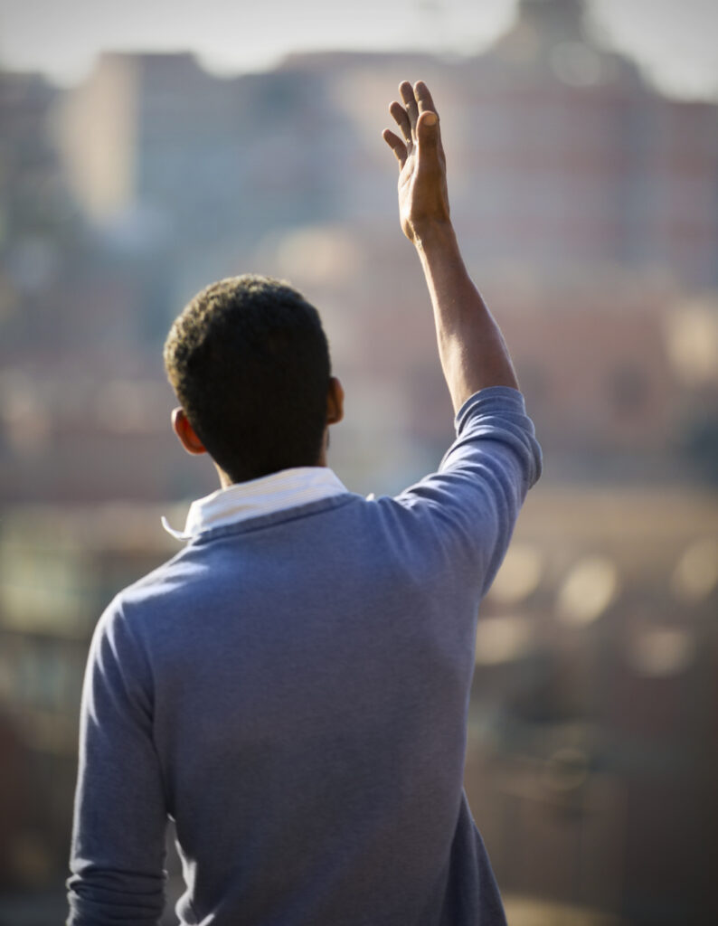 man standing with his arm raised facing a city