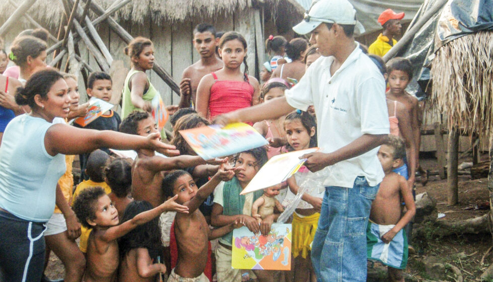 Boy hands out book to children in a village