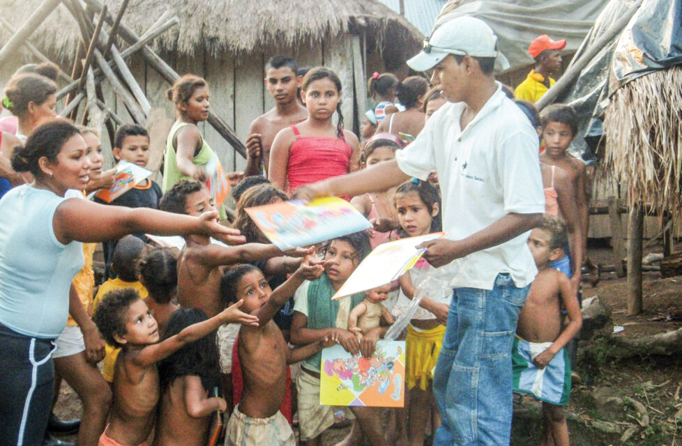 Boy hands out book to children in a village