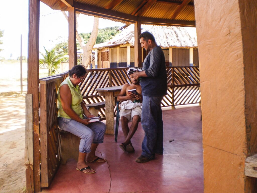 man reads the bible to two other people outside 