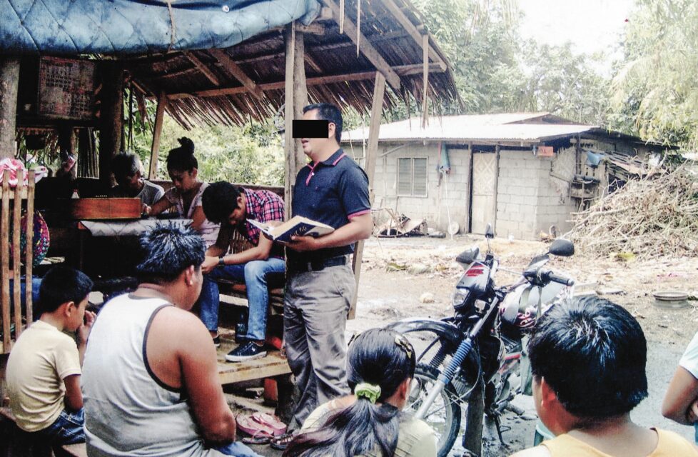 a man reads the bible to a group of men outside in their village