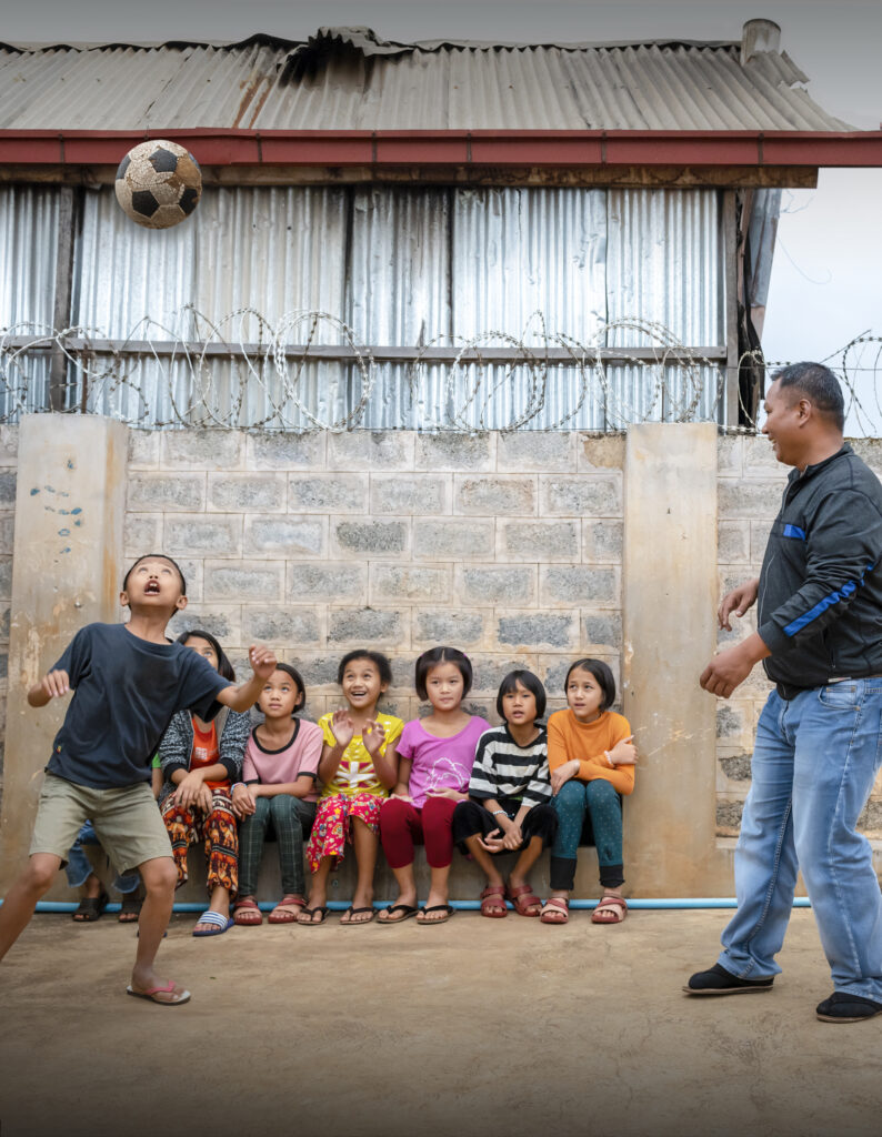 Myanmar child and adult play soccer in front of wall