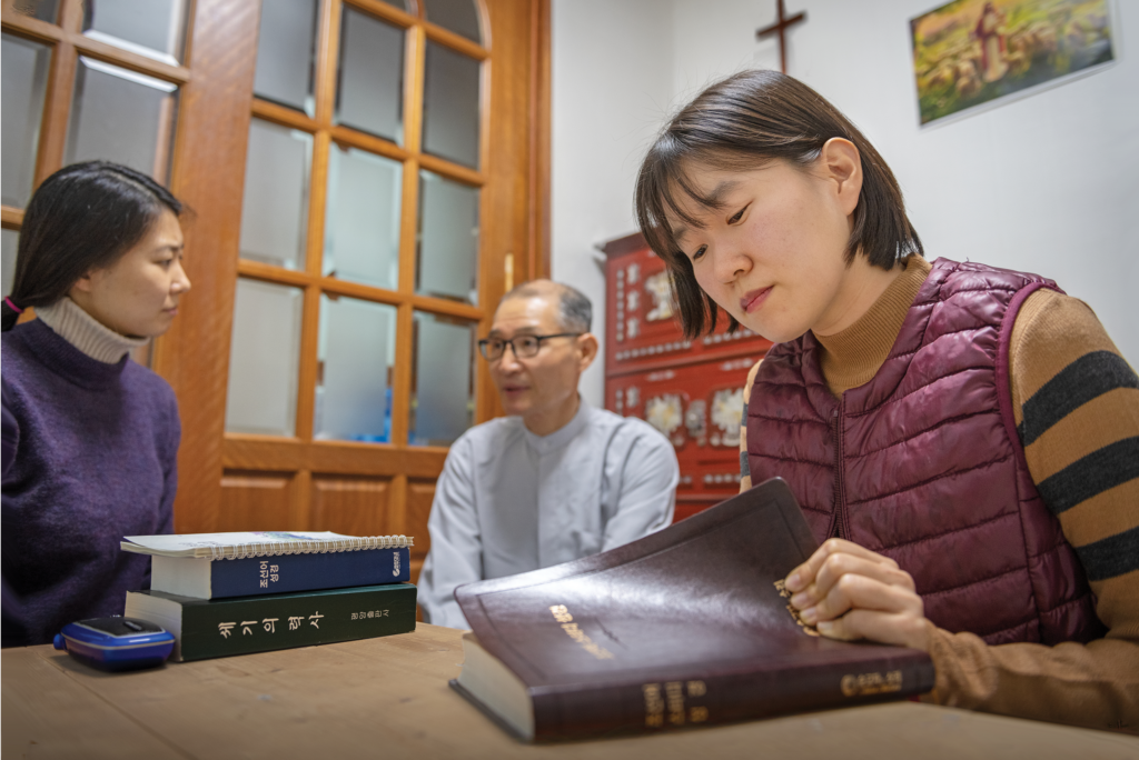 North Korean women and man sit at table reading bible