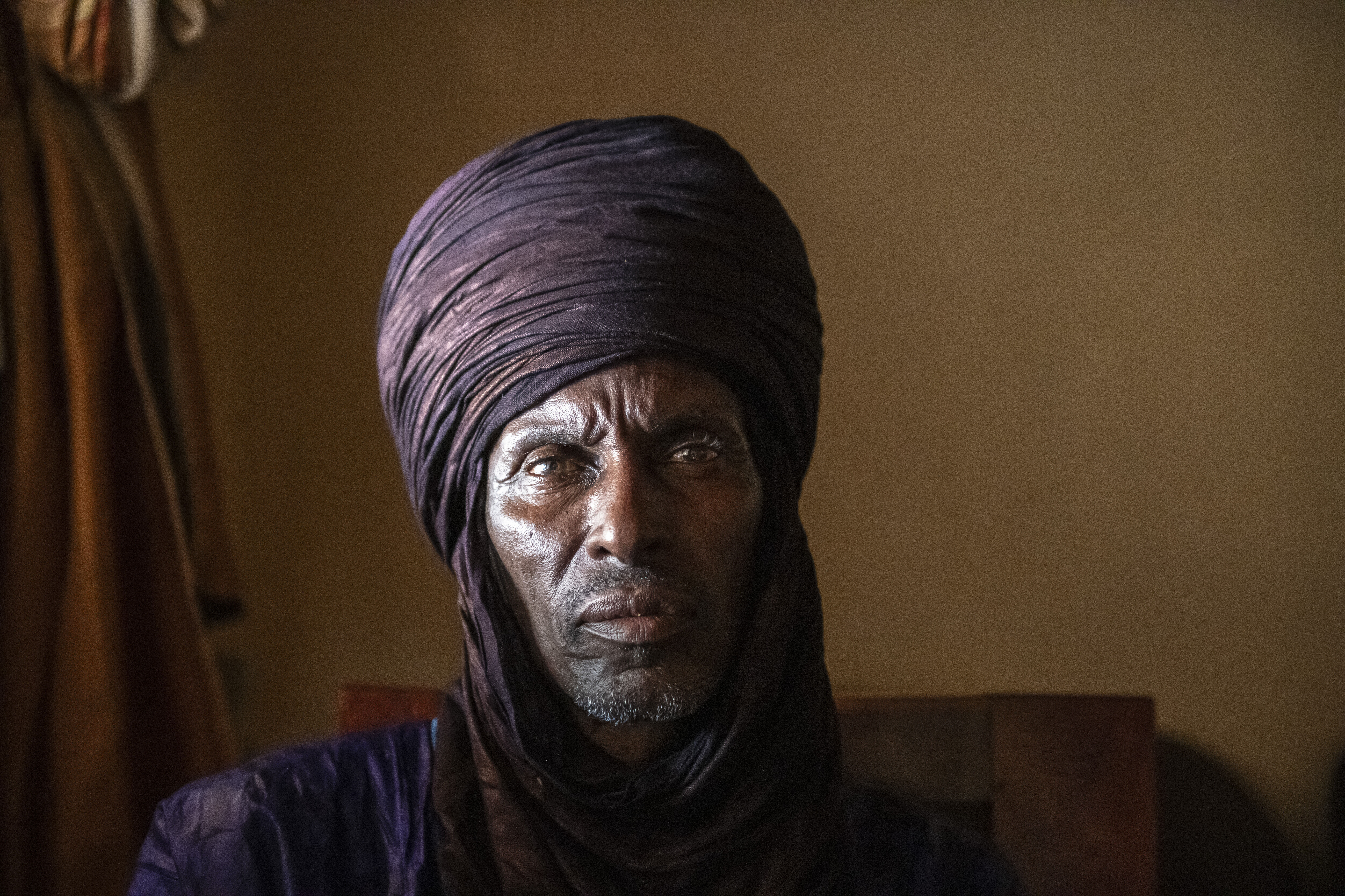 A Fulani man wearing a traditional head covering looks into the camera